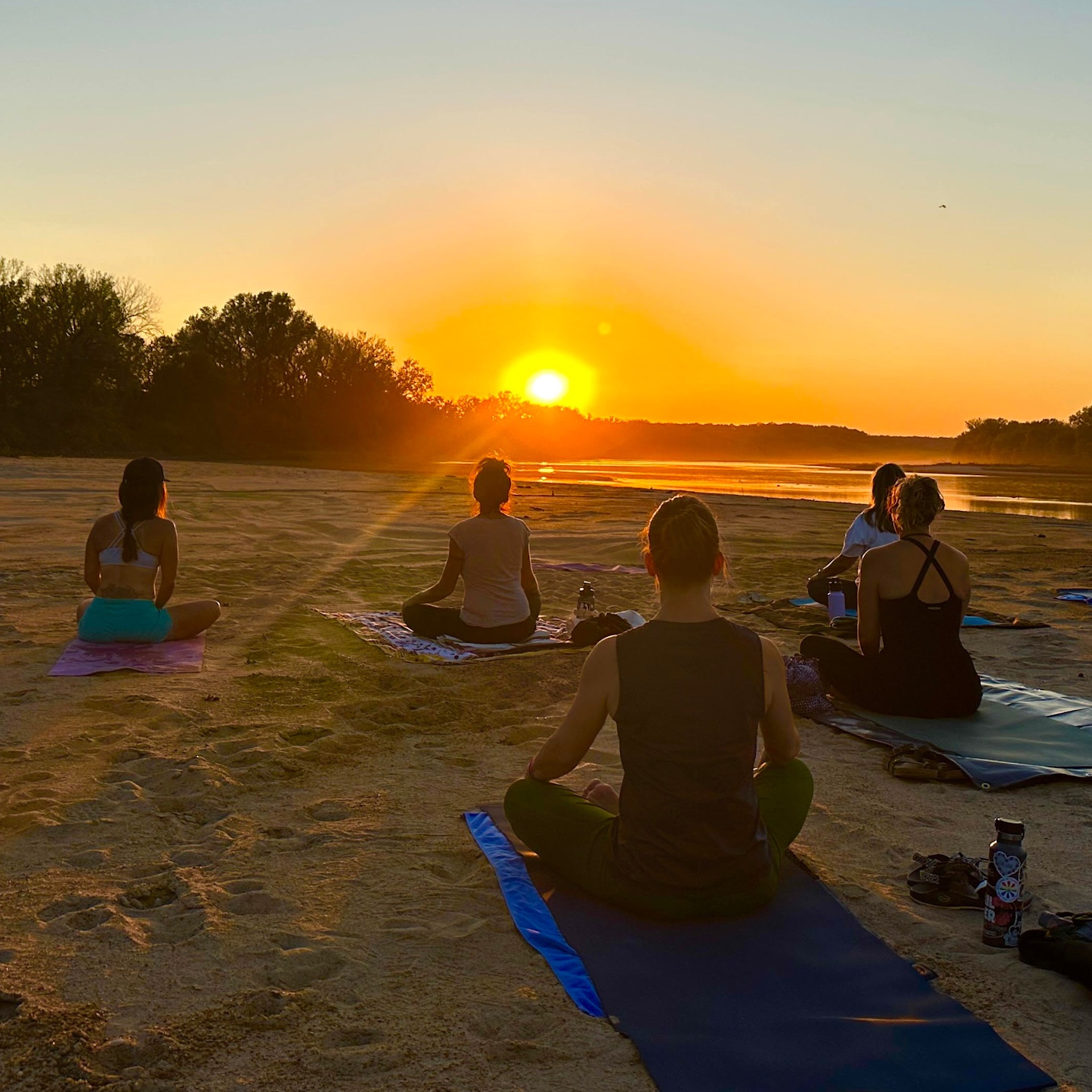 Group seated in meditation by the water at sunset